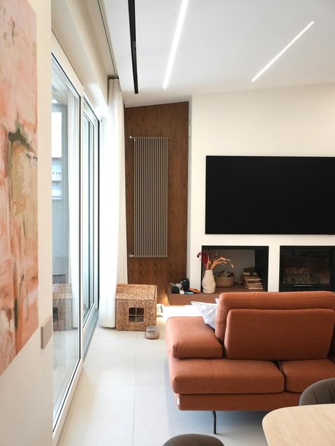 Soggiorno moderno con divano marrone, TV a parete, parete decorativa in legno e porte scorrevoli in vetro a tutta altezza.