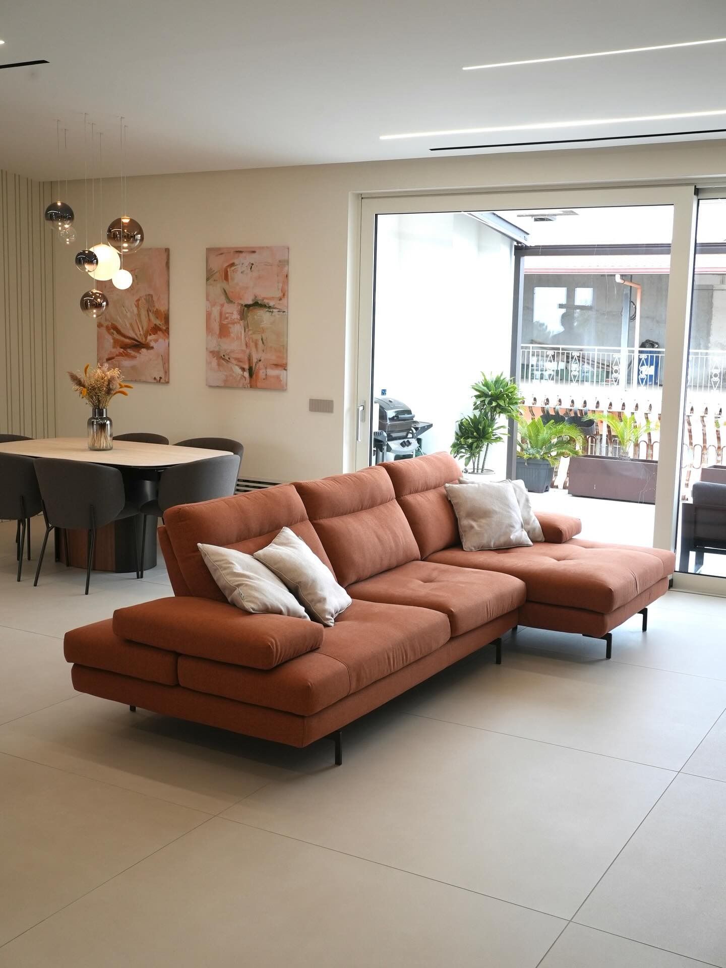 Soggiorno moderno con divano componibile in terracotta, tavolo da pranzo e porte finestre che si aprono sul balcone.