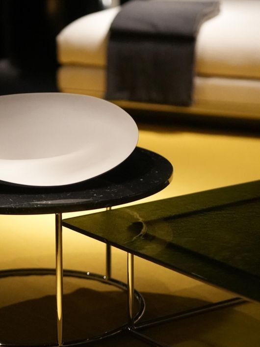 Tavolino da caffè moderno con piano bianco e superficie nera in una stanza illuminata da luci calde.