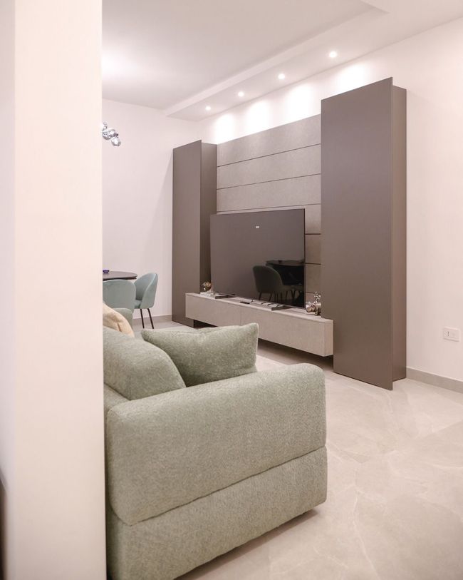 Soggiorno moderno con divano verde, mobile TV a parete e pavimento piastrellato di colore chiaro.