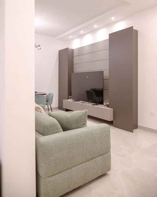 Soggiorno moderno con divano verde chiaro, mobile TV a parete e pareti bianche con illuminazione a incasso.