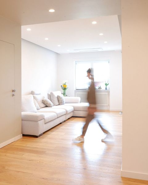 Luminoso soggiorno moderno con divano bianco, pavimento in legno e una persona sfocata che lo attraversa.