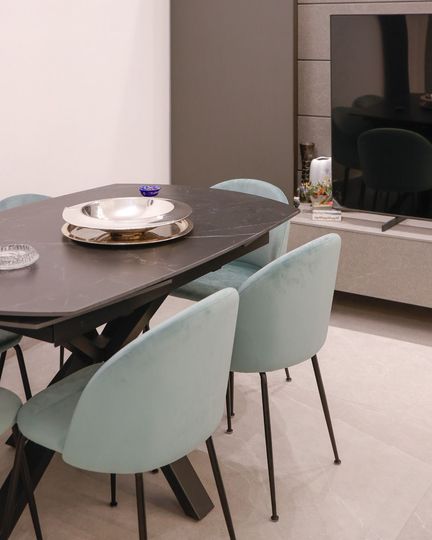 Sala da pranzo moderna con tavolo scuro, sedie color menta e mobile porta TV sullo sfondo.