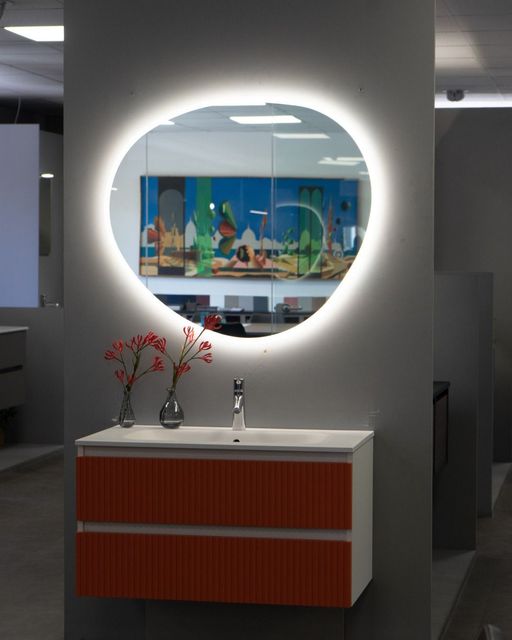 Specchio rotondo a parete con luce diffusa sopra un piccolo armadietto in un corridoio di un ufficio moderno.