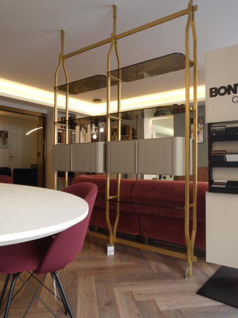 Salotto moderno con divani color bordeaux, tavolo rotondo, pavimento in legno e divisorio a parete con specchio e cornice dorata.