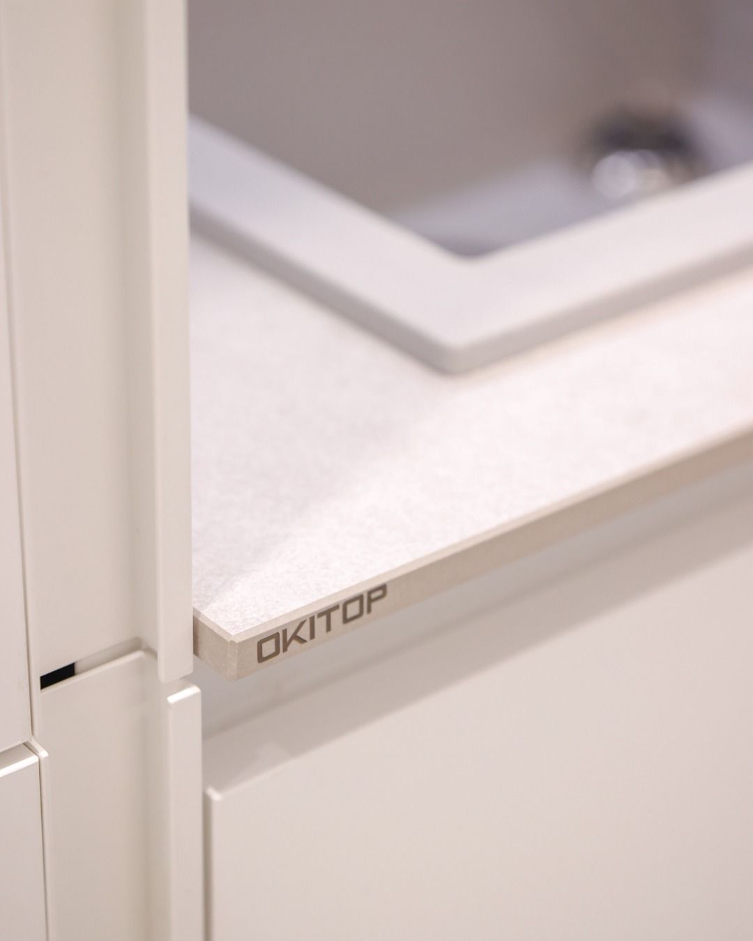 Primo piano di un mobile lavabo bianco con il logo OKITO e un piano d'appoggio chiaro.