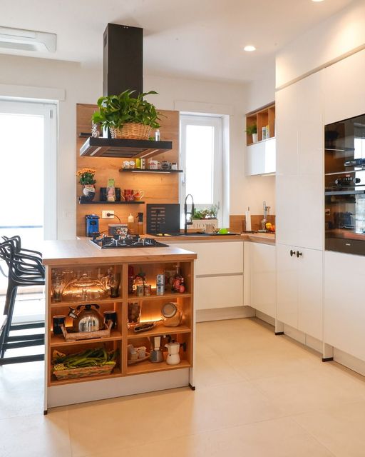 Cucina moderna con isola, mobili bianchi, mensole in legno e cappa aspirante nera.