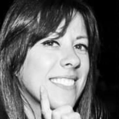 Ritratto in bianco e nero di una persona sorridente, con un dito appoggiato al mento.