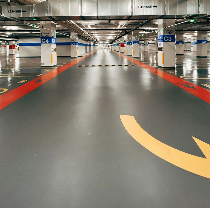 An empty, modern parking garage with gray floors, red lane markings, yellow arrows, and white pillars labeled with codes.