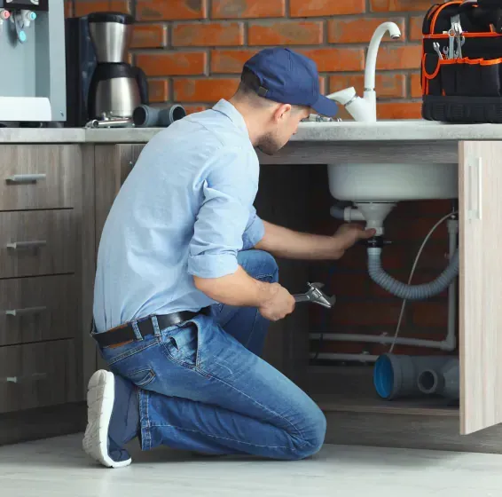 A plumber is fixing a sink in a kitchen with a wrench.