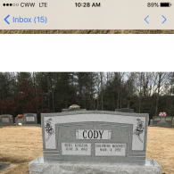 A gray granite headstone for the Cody family in a cemetery, featuring two names and dates engraved on the front.