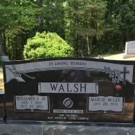 Black granite headstone for the Walsh family in a cemetery, featuring two engraved name panels, a plow, and a cross.