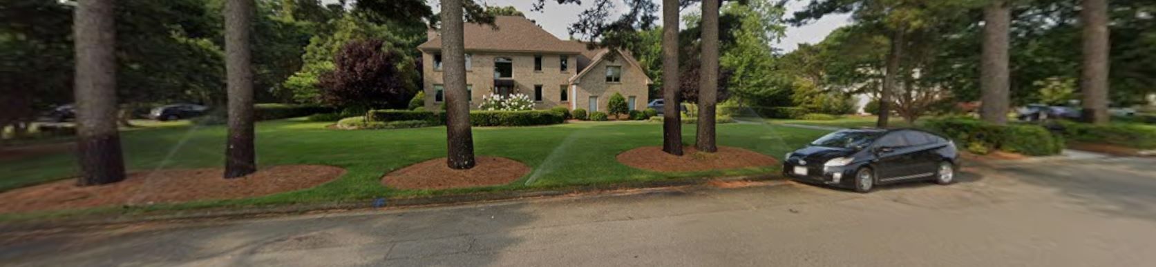 Suburban street with a dark car parked by trees and a house in the background