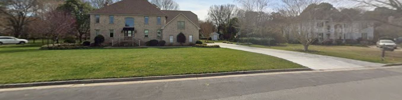 Large stone building with arched windows beside a green lawn and curved driveway under a cloudy sky