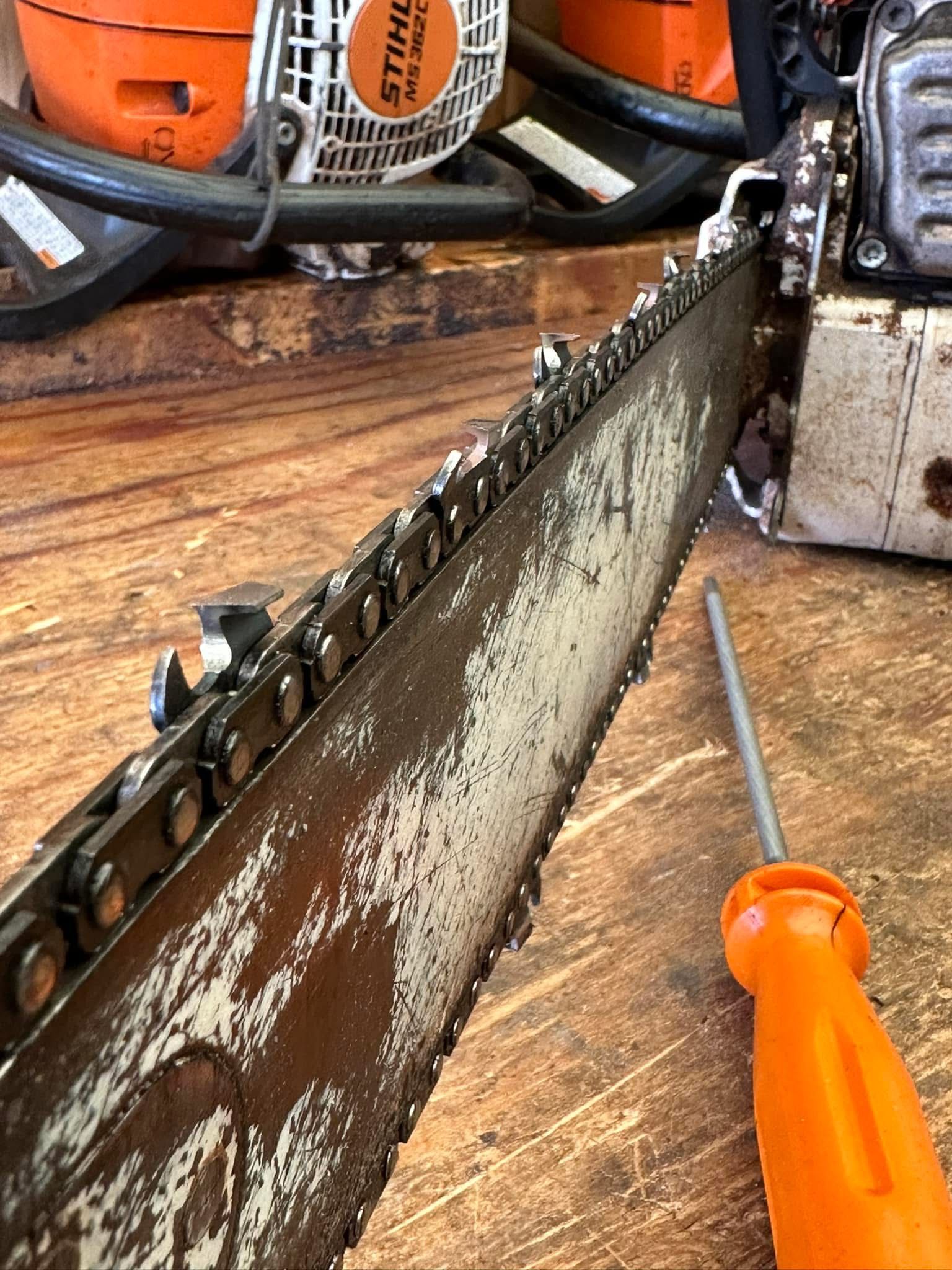 Close-up of a chainsaw blade and bar on a wooden workbench with an orange-handled screwdriver nearby