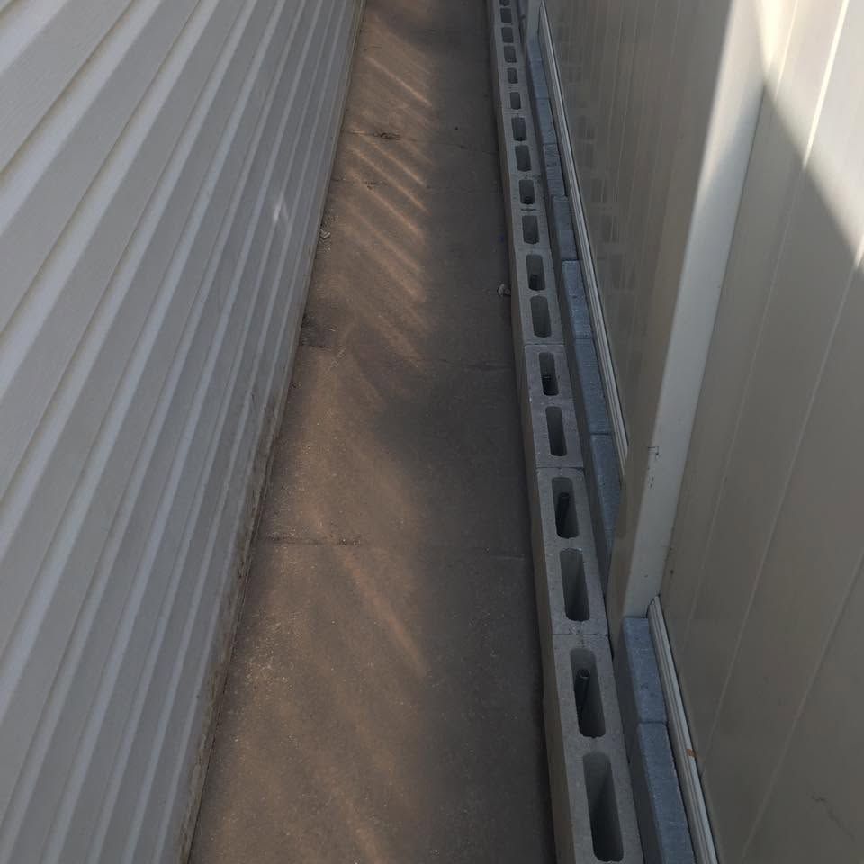 Narrow outdoor passage between white walls with a concrete floor and metal drainage channel