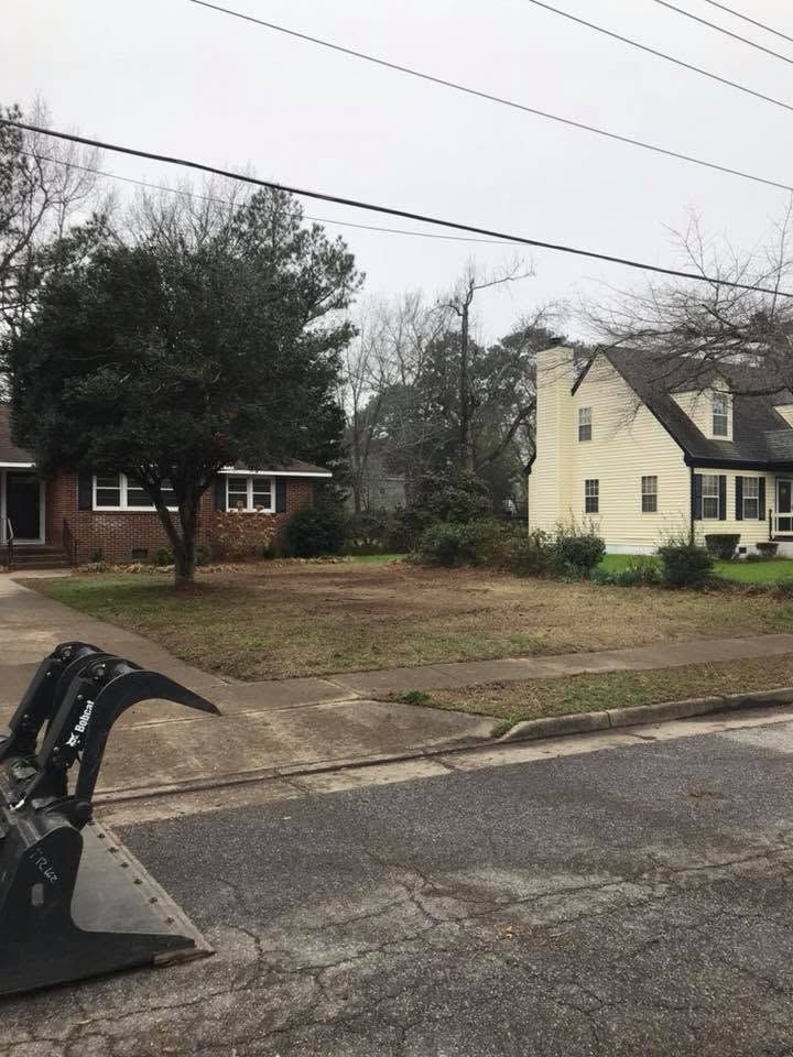 Street view of two houses on an overcast day, with a bulldozer bucket in the foreground.