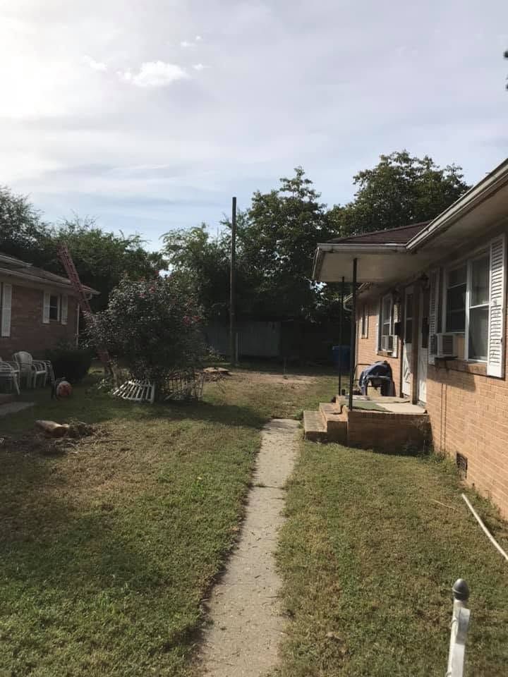 Narrow concrete path through a grassy backyard between two houses, with porch and fence in view.