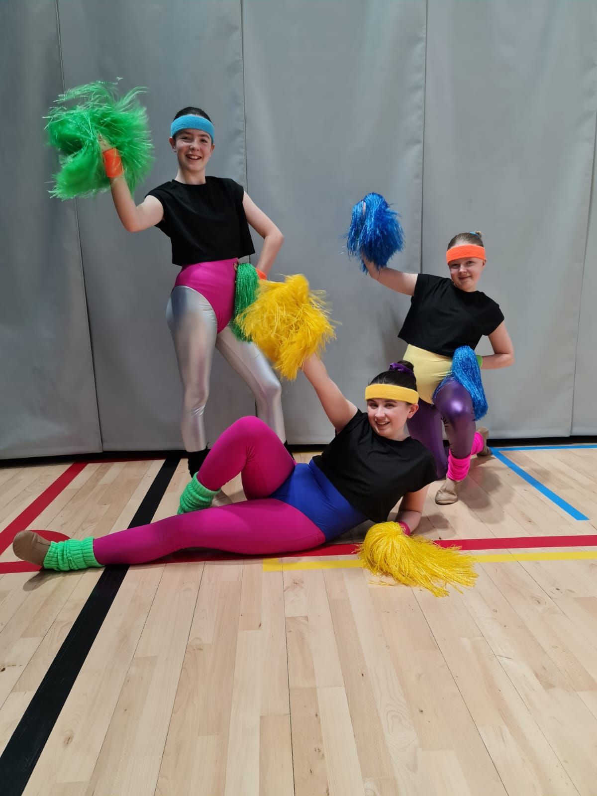 Three girls lying on the floor and staying in fun positions with pom poms on their hands. Pom-Poms are colorful.