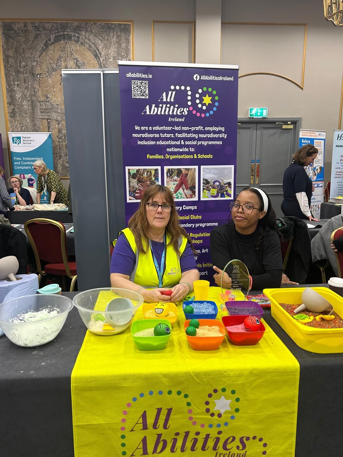 The All Abilities Ireland stand at the festival and two women sitting at a table.