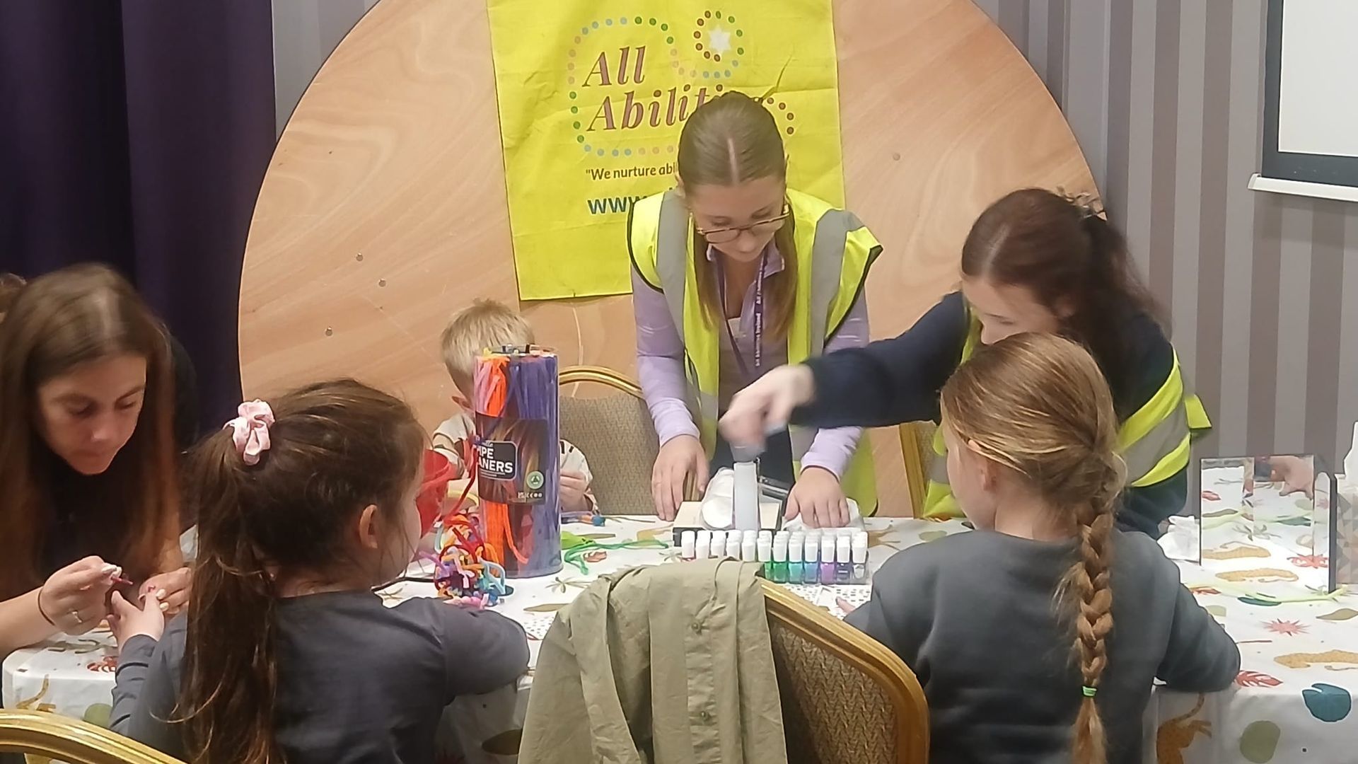The girls are standing by a table, choosing nail polishes to paint the nails of children who would like that.