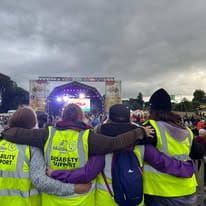 People in workers' vests have their hands behind each other's backs in a friendly manner and are looking at the stage.
