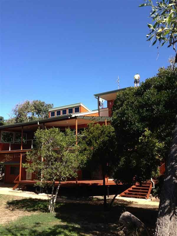 A Wooden Building on a Hill With a Deck and Surrounding Trees — Vision Roofing Fascia & Gutter in Hervey Bay, QLD
