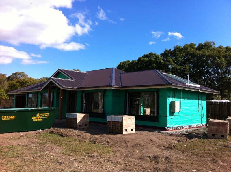 House Under Construction With a Dark Roof and Green Wrap — Vision Roofing Fascia & Gutter in Hervey Bay, QLD