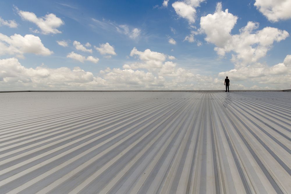 A Person Stands on a Vast, Corrugated Metal Surface — Vision Roofing Fascia & Gutter in Hervey Bay, QLD