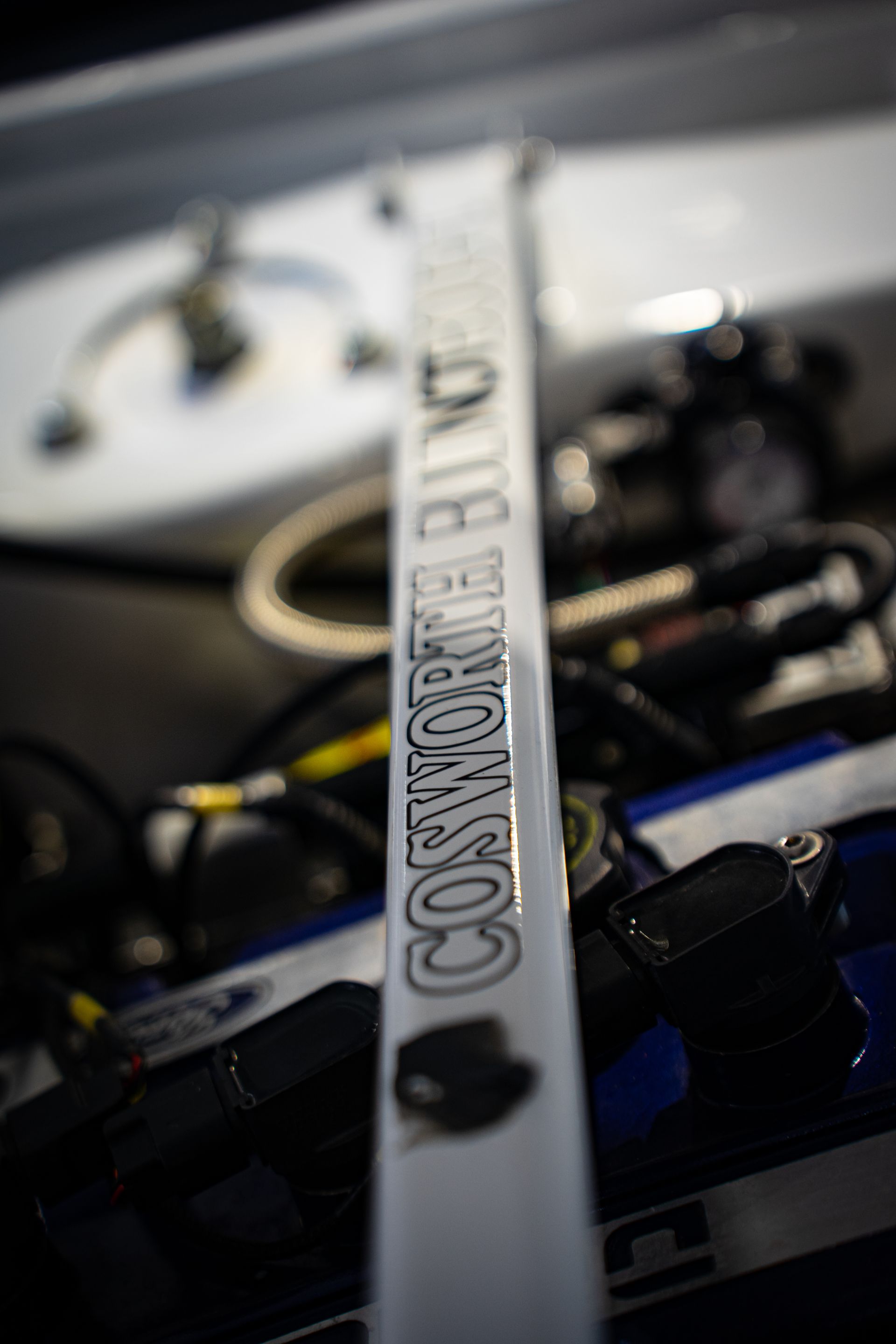 A close-up of a white strut bar in an engine bay, with the text 