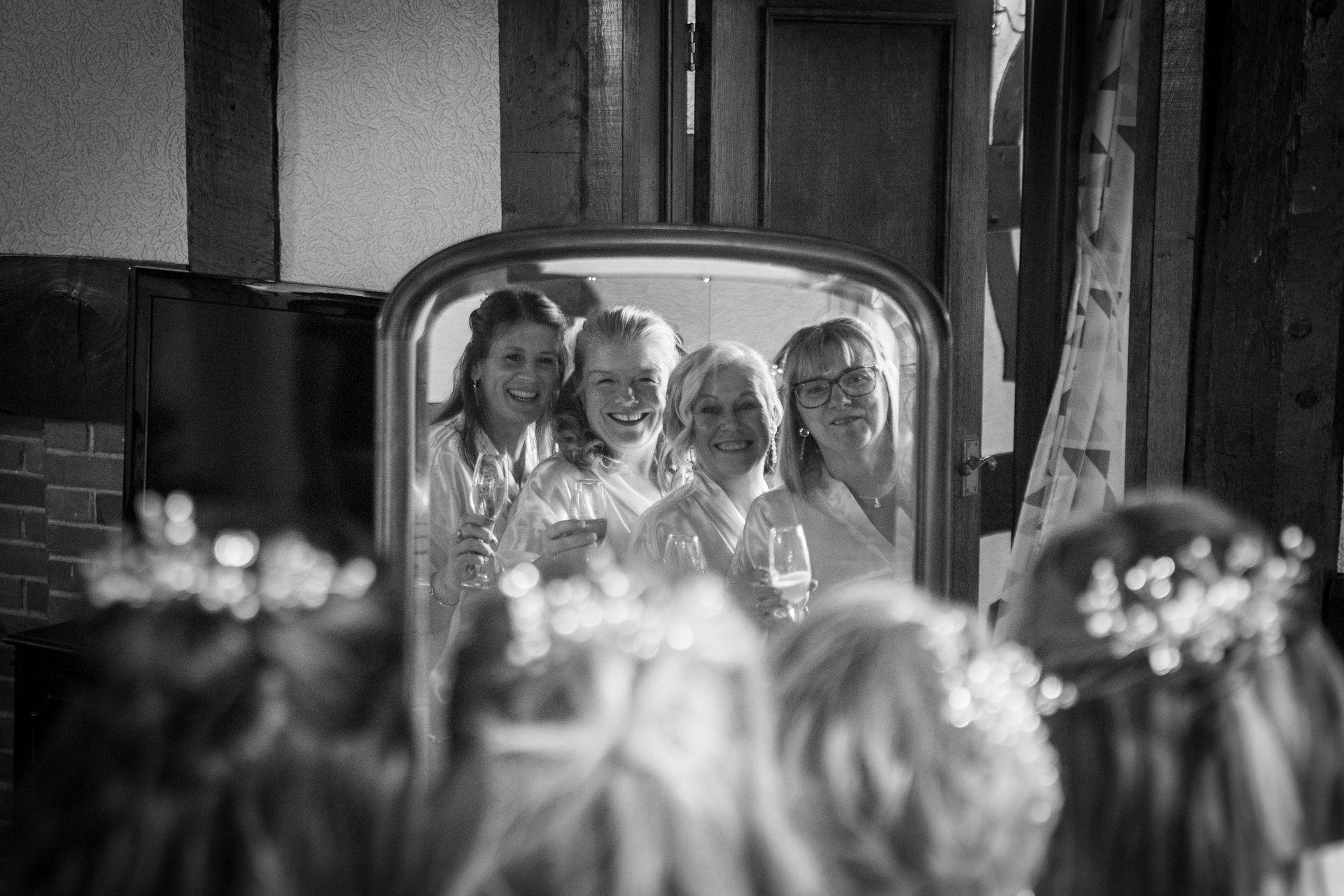 Bridesmaids in the mirror, toasting with champagne. They are smiling in a wooden room.