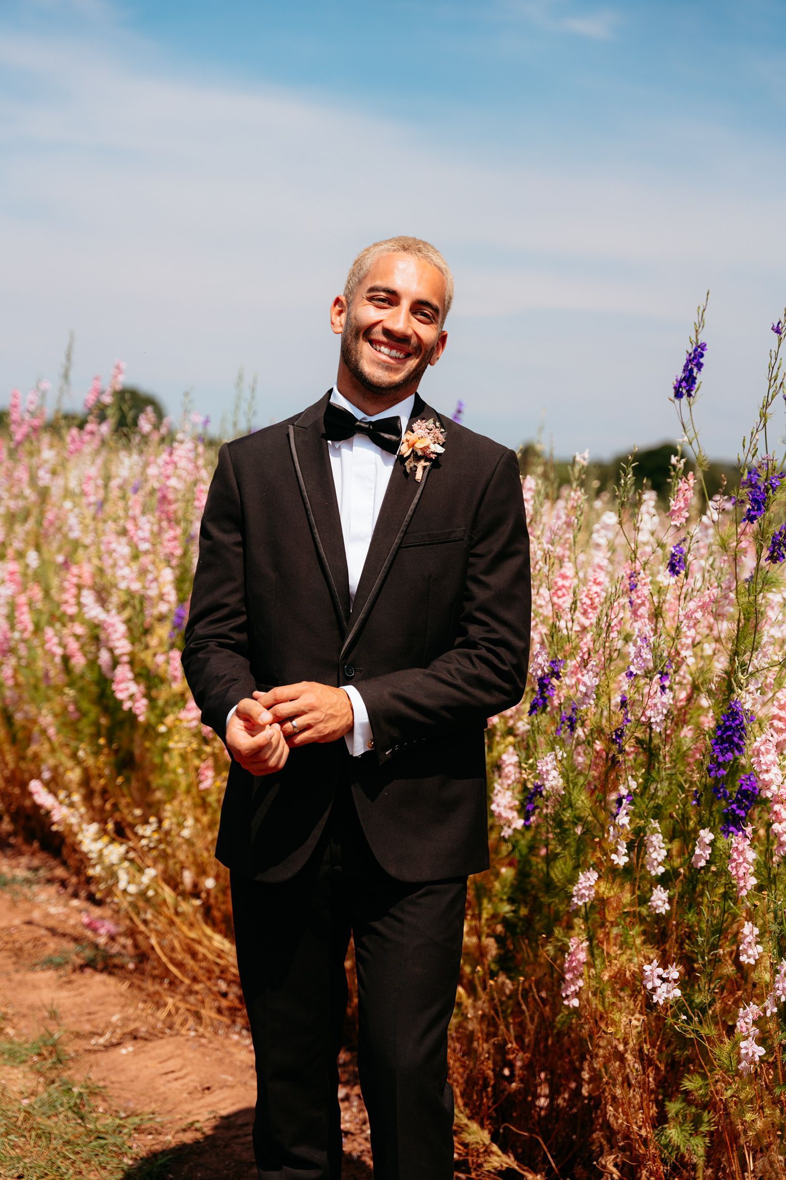 Couple smiles for the camera, outdoors. Woman with blonde hair, white dress, man in suit, green tie. Scenic background.