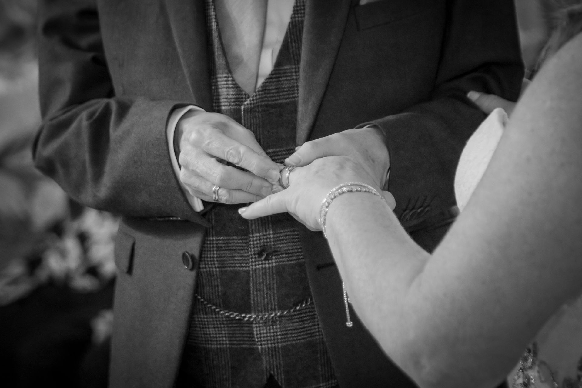 Groom placing a ring on bride's finger during a wedding ceremony. Black and white.