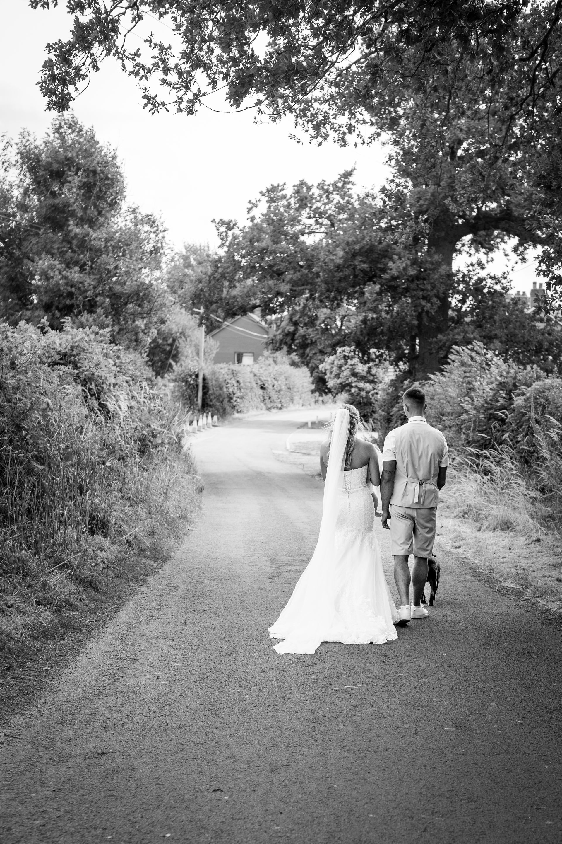 Bride and groom walk hand-in-hand on a path. Black and white photo in a wooded area.