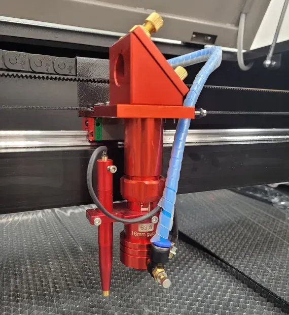 Red laser cutting head on a black laser cutter machine. Blue tube provides air assist to the nozzle.