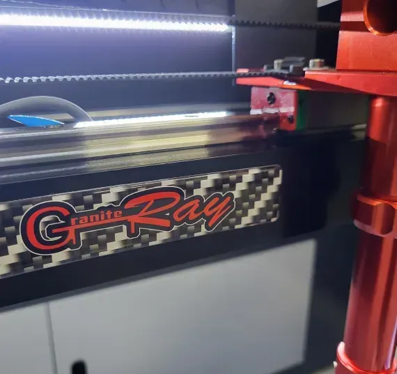 Granite Ray machine with logo on a black surface, red and silver accents. Illuminated by a bright light.