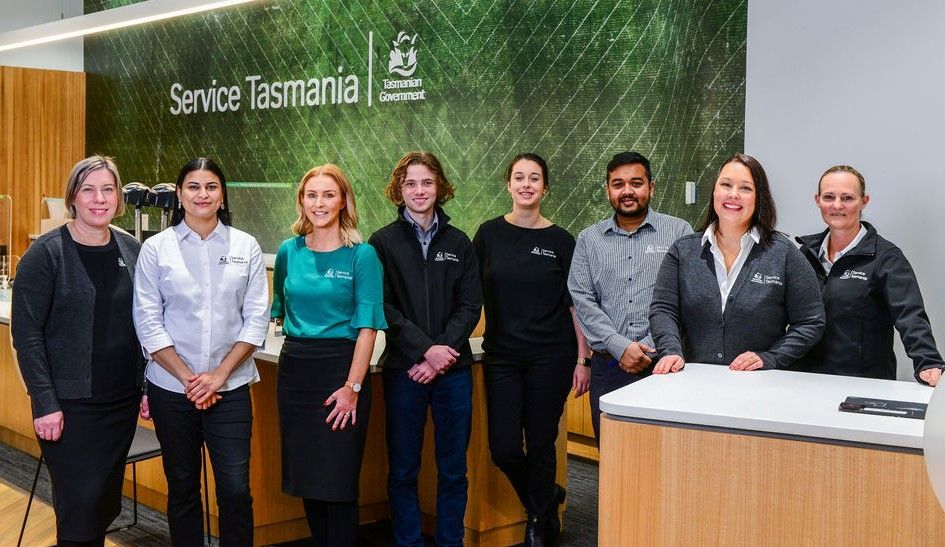 Group of Service Tasmania employees standing at a counter. Service Tasmania logo on the wall behind them.