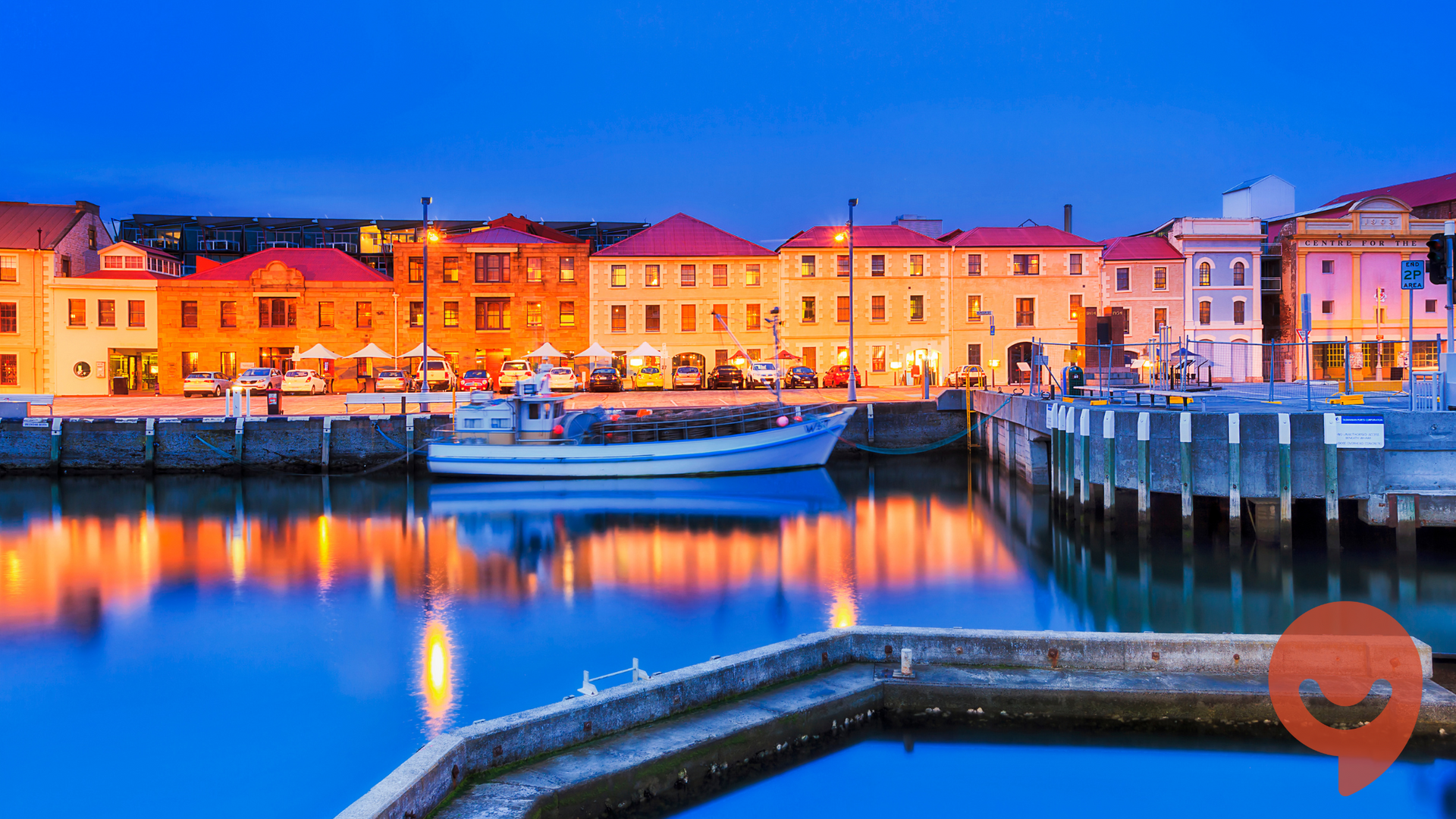 Harbor at dusk with buildings lit up, reflecting in calm water. Tasmanian landscape
