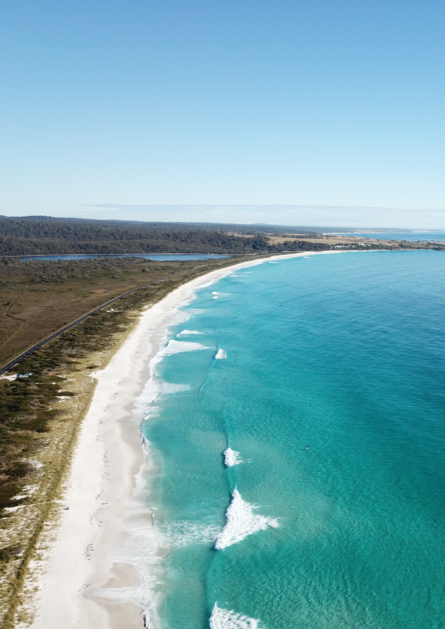 Turquoise ocean waves rolling onto a white sand beach under a clear blue sky.