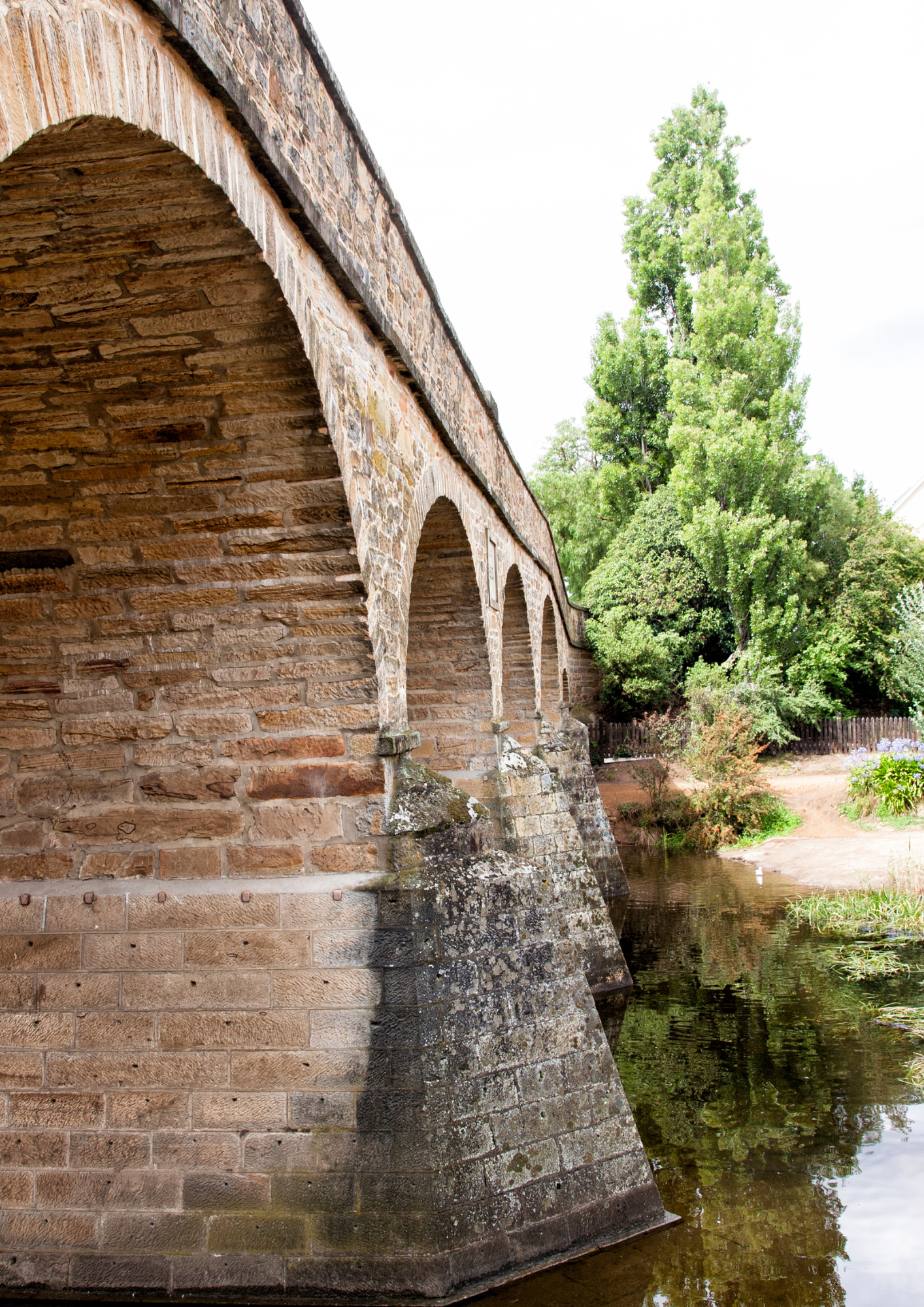 Stone arch bridge over calm water, trees in background.