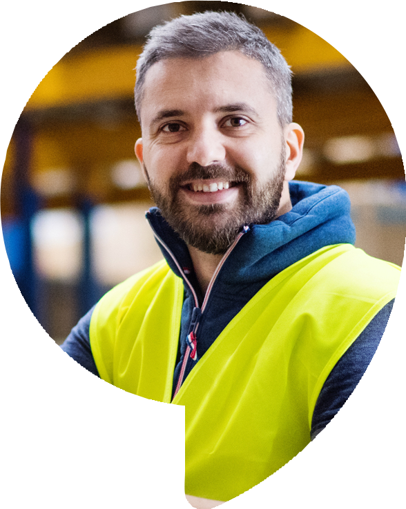 Man wearing a safety vest smiles in a warehouse setting.