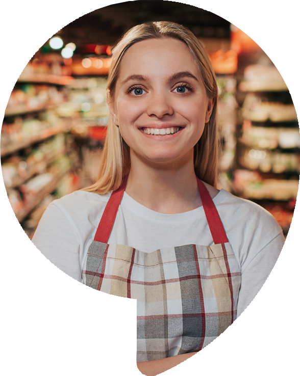 Woman in apron smiling in a grocery store.