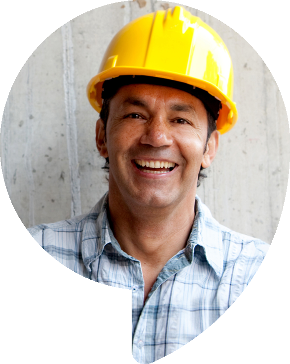 Construction worker smiling, wearing yellow hard hat and plaid shirt, against a concrete background.