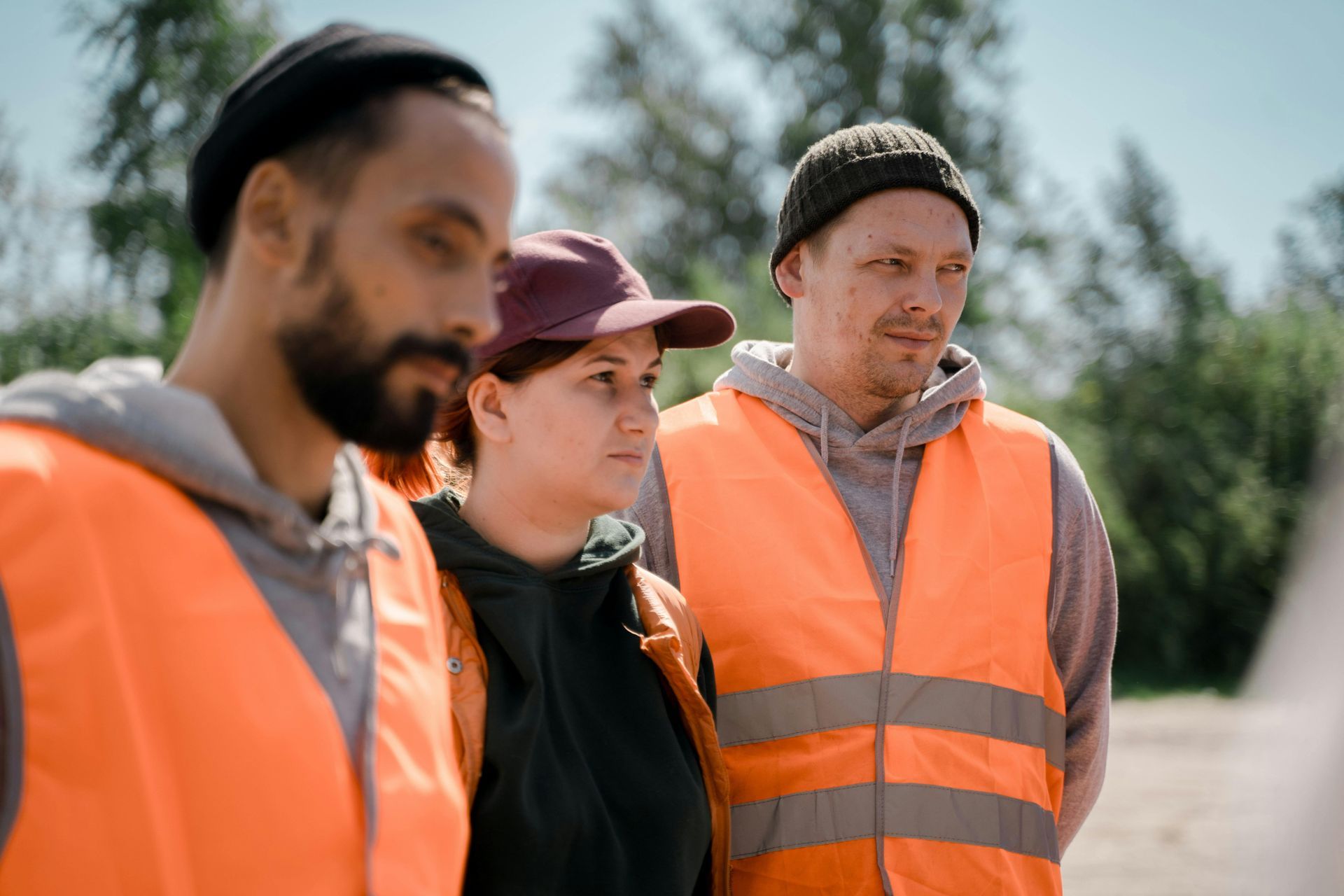 Three people wearing orange safety vests, standing outside.