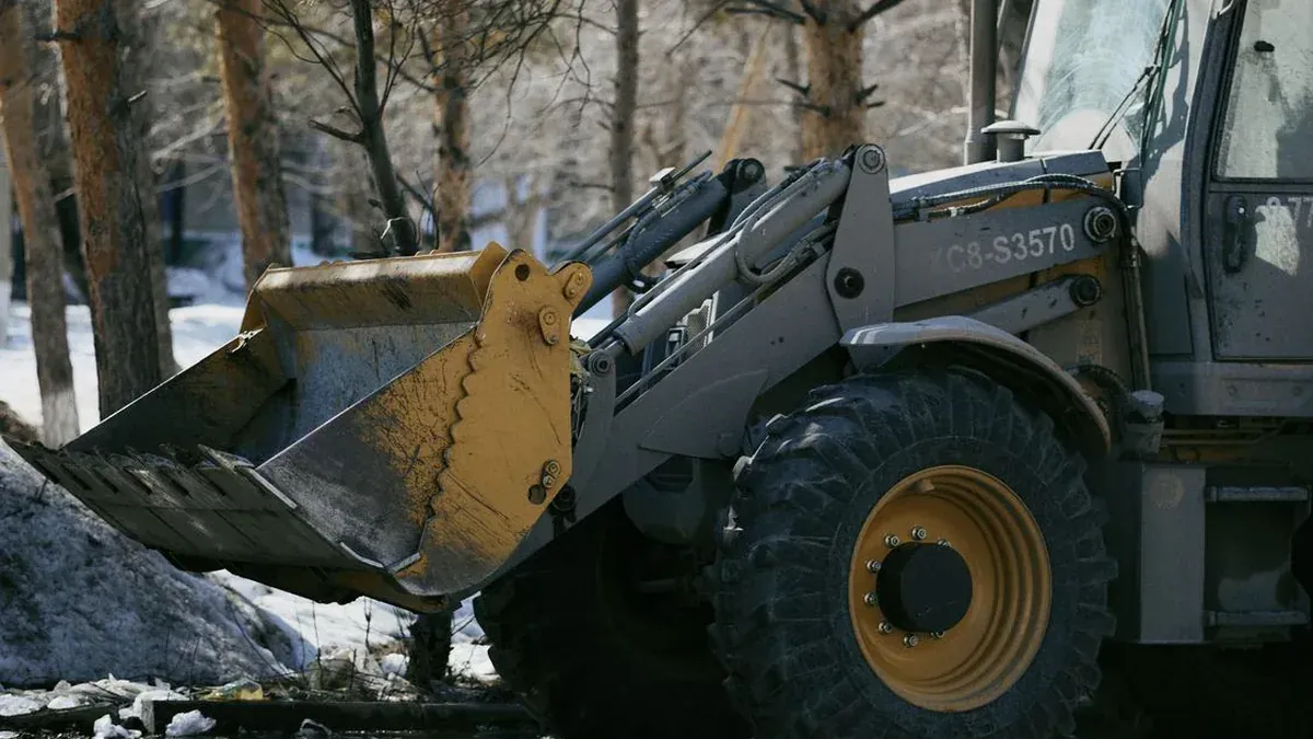 Excavator working beside snow-covered trees in winter