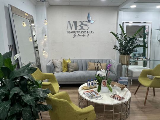 A waiting room with a couch , chairs , a table and a mirror.
