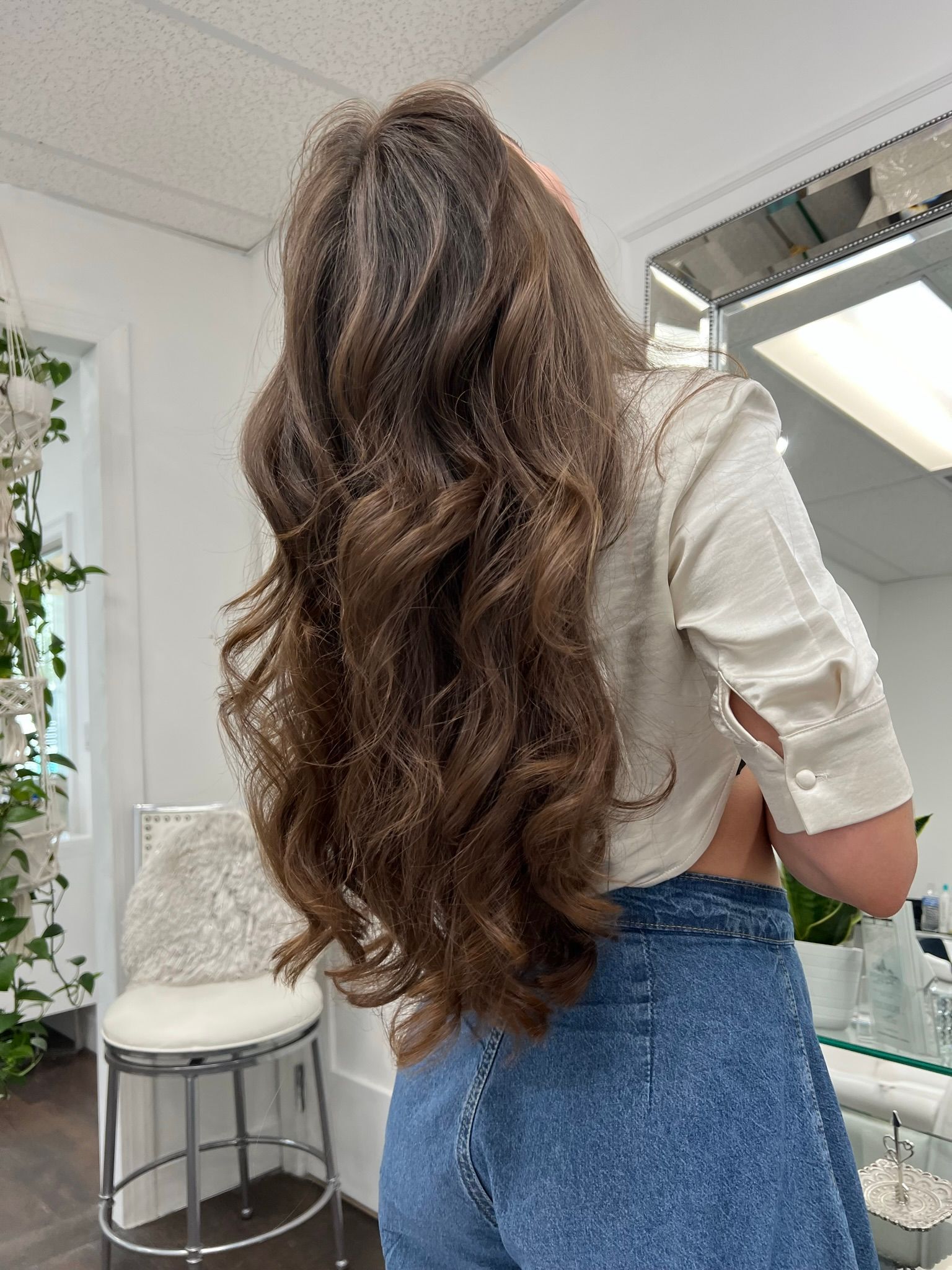 A woman with long brown hair is standing in a room wearing jeans and a white shirt.