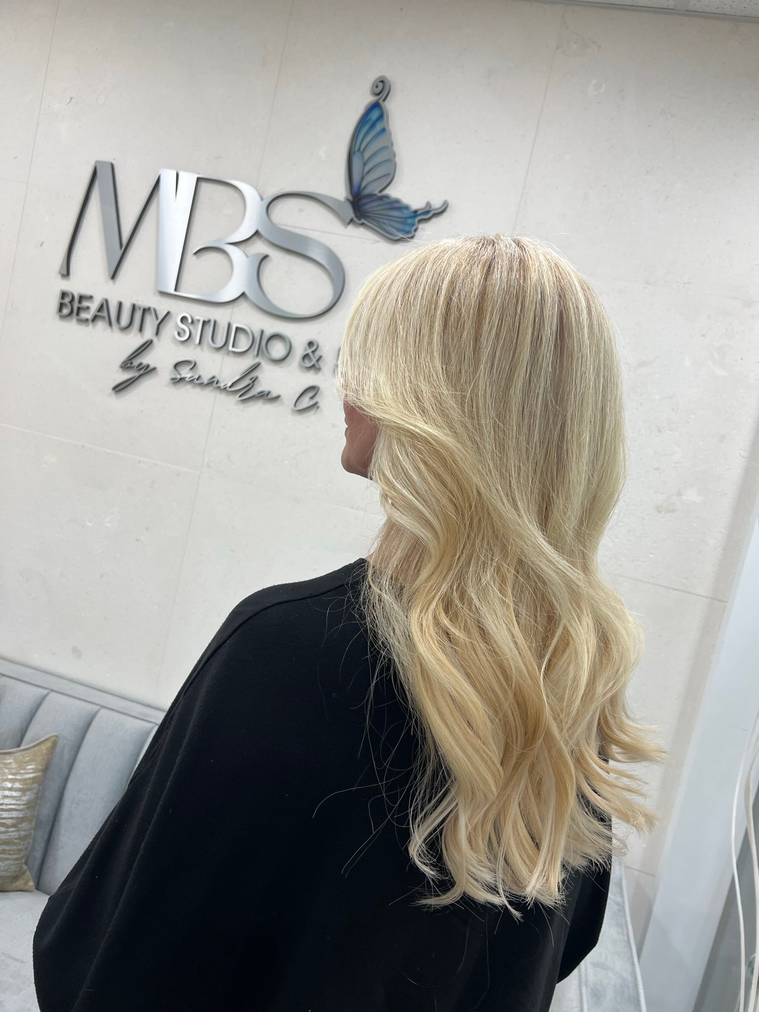 A woman with blonde hair is standing in front of a mbs beauty studio and salon.