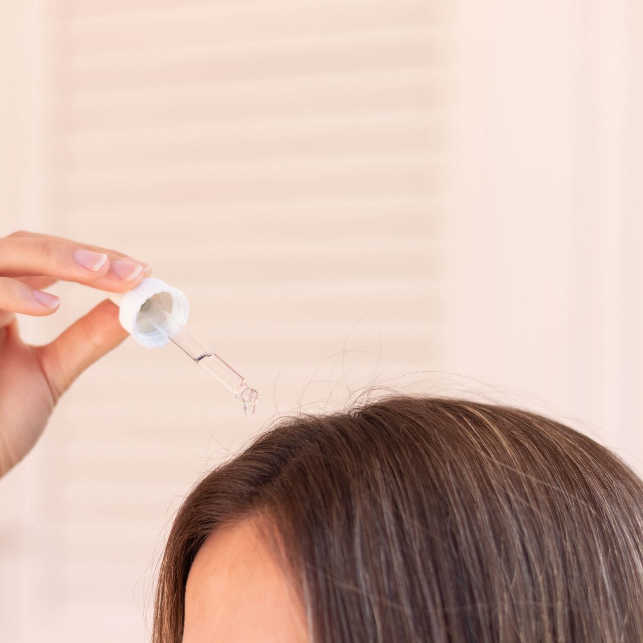 A woman is applying a dropper to her hair.