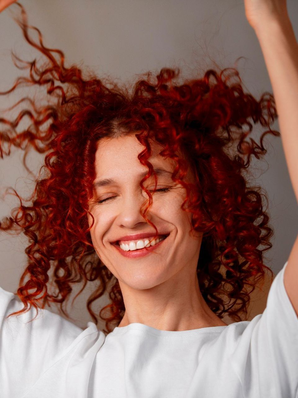 A woman with red curly hair is smiling with her arms in the air.